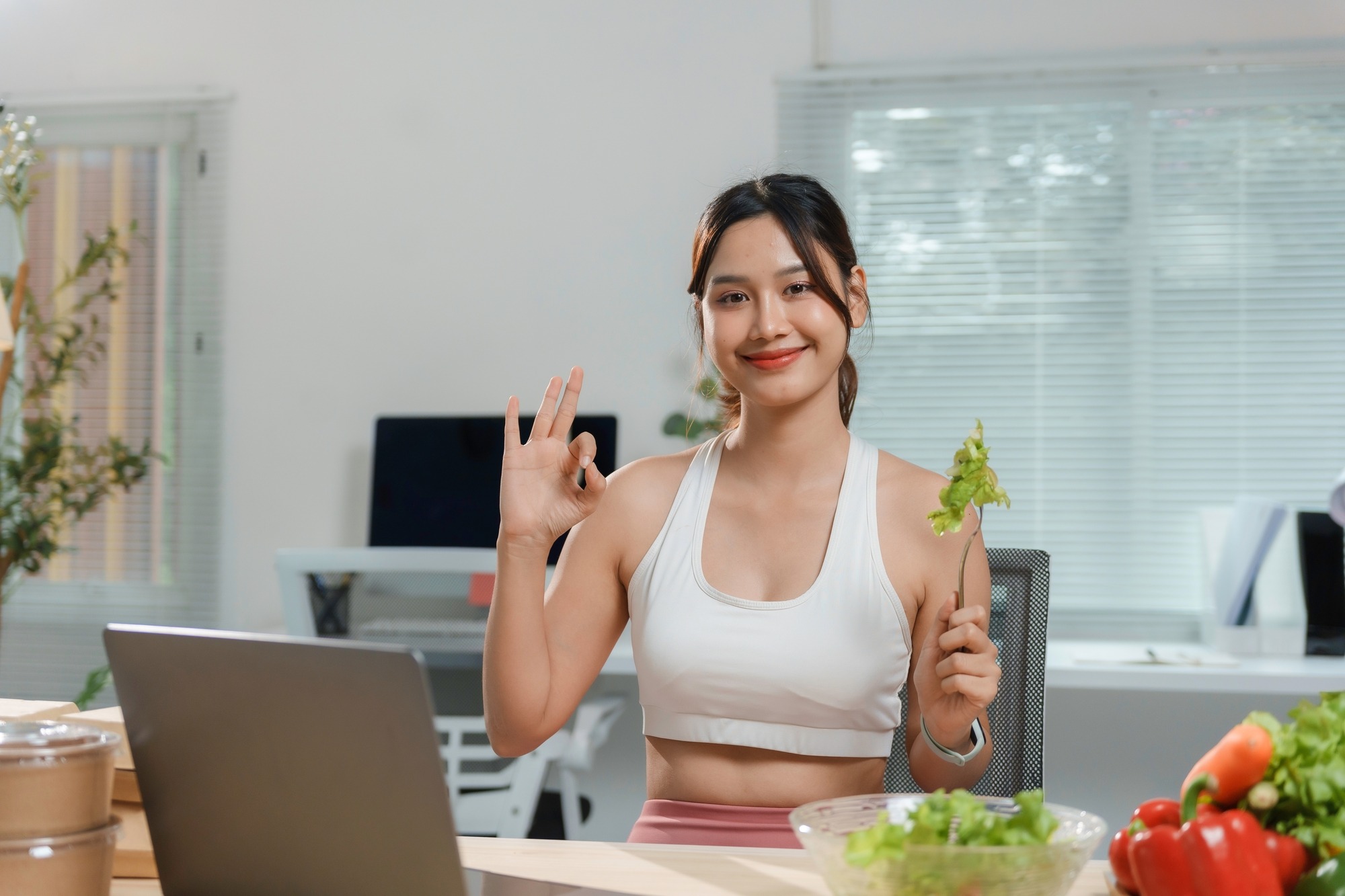 Asian Nutritionist Showing Ok Sign While Eating Healthy Salad in a Video Call About Healthy Eating Habits and Online Fitness Training.